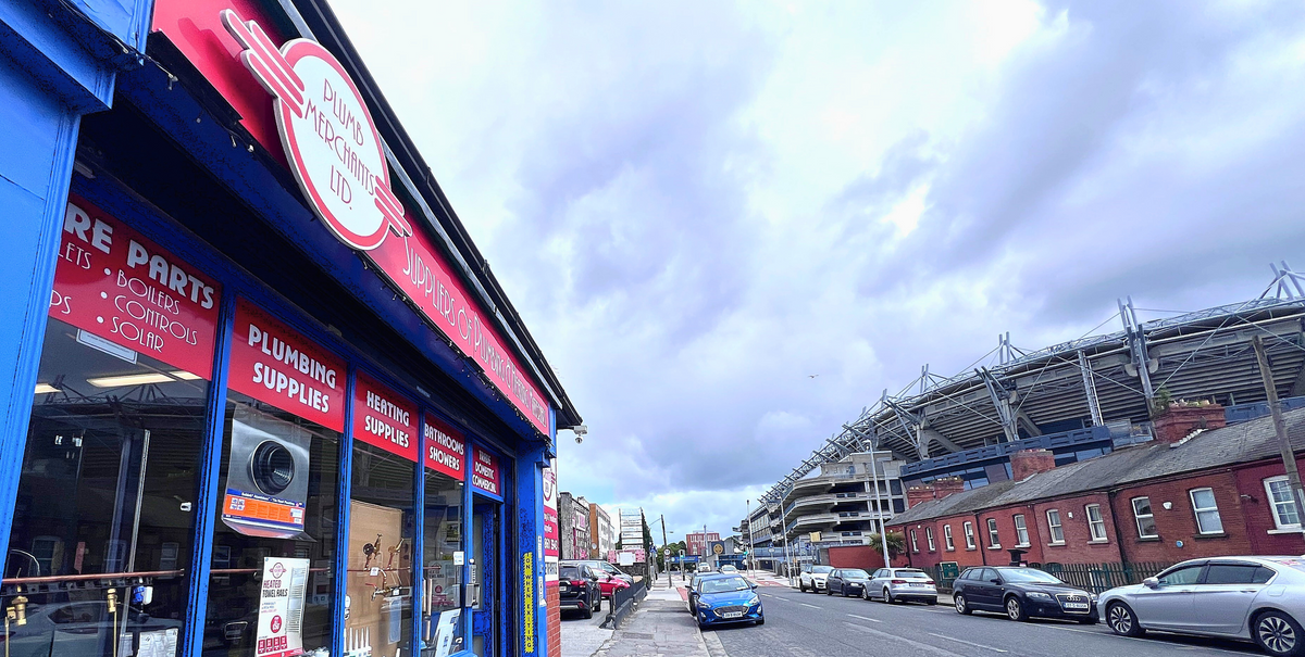 Street view with a plumbing supply store and a large stadium in the background.